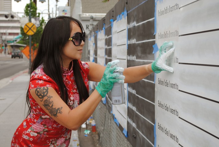 Artist Candy Chang spray painting stencil with "Before I did I want to _______" repeated on multiple rows